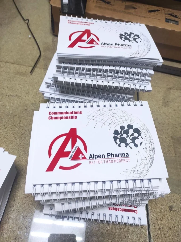 Стоси брошур Alpen Pharma з білими обкладинками та металевою пружиною вздовж верхнього краю