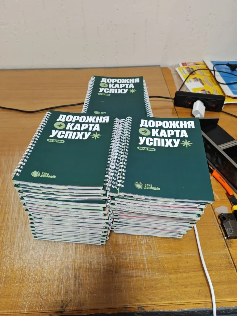Стоси видань «Дорожня карта успіху» із зеленими обкладинками та білою металевою пружиною